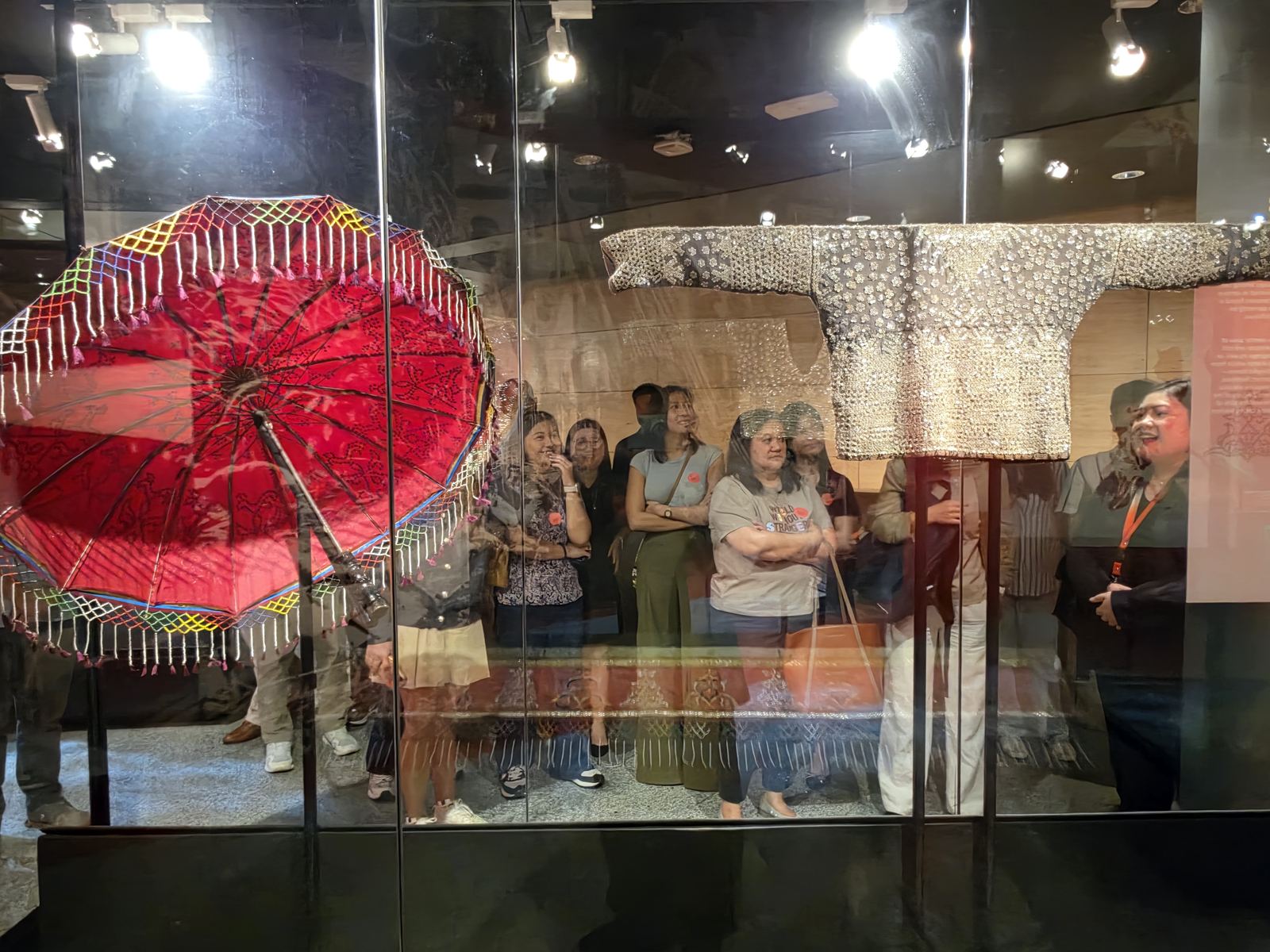 OSL lawyers viewed through a display case with a beaded umbrella and embroidered garment